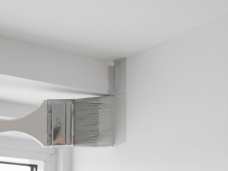 An angled paintbrush creating a perfectly straight cut-in line along a ceiling.