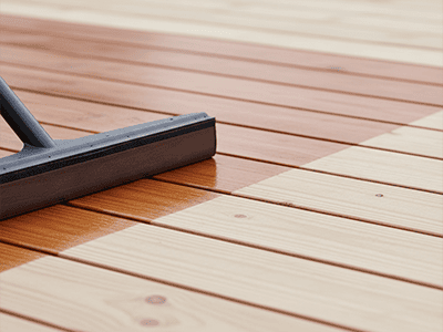 A deck staining applicator pad applying a rich timber stain to prepared deck boards.