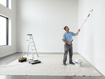 A professional painter in uniform working efficiently on a large, high-ceilinged room.