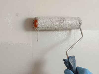 A paint roller applying a fresh, even coat of paint over a lightly sanded wall.