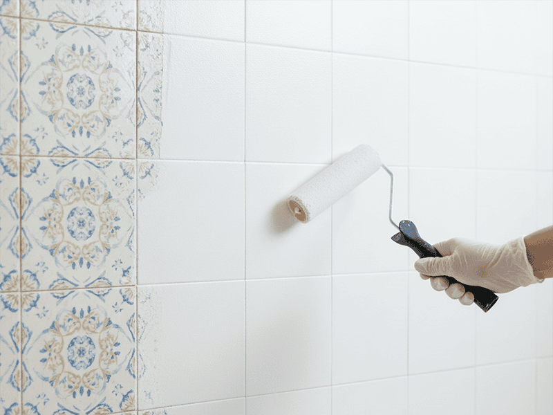 A bathroom wall showing a clear before-and-after of old tiles being painted white.