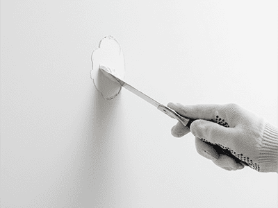 A putty knife applying filler smoothly into a crack on a plasterboard wall.
