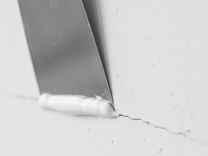 A putty knife applying filler to a small hole in a white plasterboard wall.