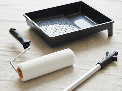 A quality paint roller, a medium-nap cover, a tray, and an extension pole on a drop sheet.