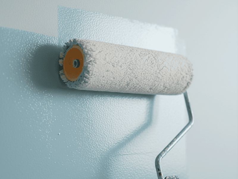 A paint roller applying a smooth, even coat of paint to a light blue wall.