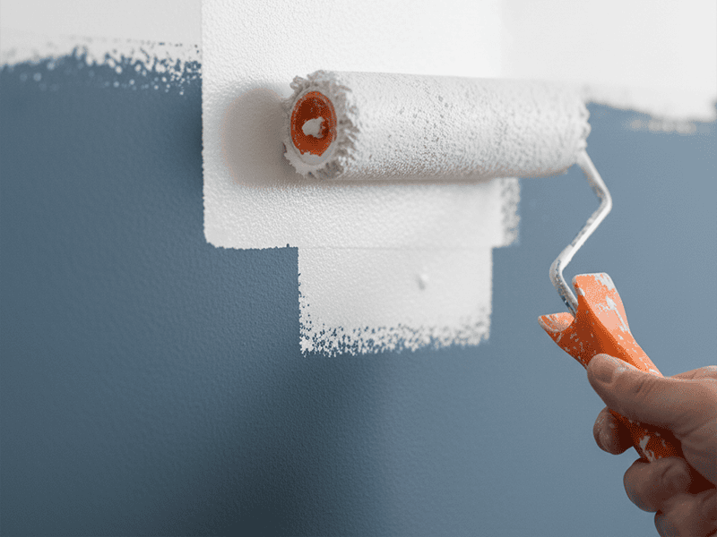 A paint roller applying a white coat of primer to a dark wall.