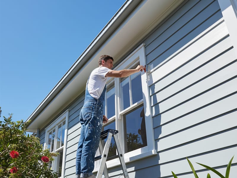 Painter on a ladder painting the exterior of a modern Australian weatherboard house.