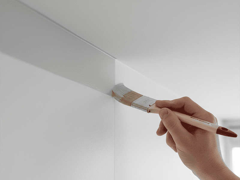 Close-up of a painter's hand using a brush to carefully cut in along the edge of a wall.